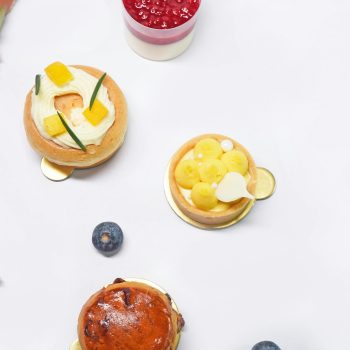 Artistic flat lay of gourmet desserts including pastries and fruit tarts on a white surface.
