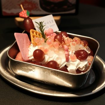 Colorful fruit ice cream dessert with whipped cream and toppings served in a metal bowl.